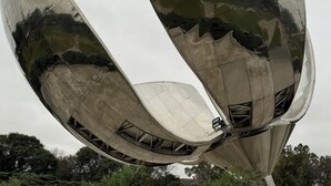 Une structure métallique aux lignes courbes, dotée d’une surface réfléchissante, et entourée de verdure.