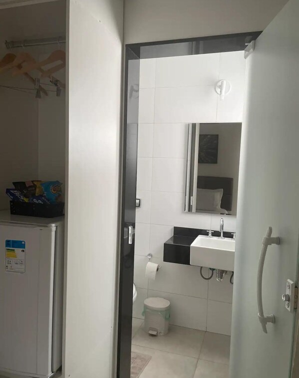 Ein Badezimmer mit Toilette, Waschbecken und Spiegel. Ein Mülleimer und ein Handtuchhalter sind ebenfalls zu sehen.