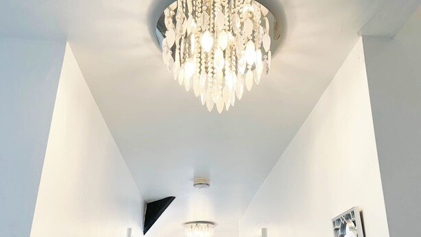 A hallway with a chandelier, a ceiling vent, and framed artwork on the walls. - Large 8 Bedroom House in Edgbaston (Birmingham)