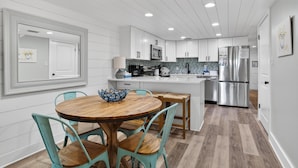 Una cocina moderna con armarios blancos, un refrigerador de acero inoxidable, una mesa de comedor de madera con sillas y un salpicadero de azulejos.