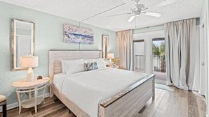 Un dormitorio con una cama grande, un ventilador de techo, un cuadro y vistas al exterior.