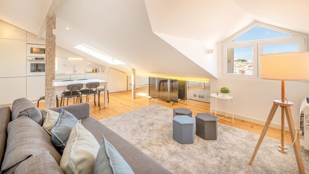 Un appartement moderne de style « loft », avec un plafond haut, un coin repas, une cuisine et une grande fenêtre offrant une vue sur la ville.
