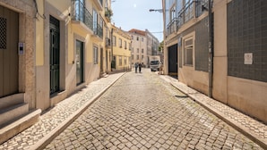 Calle adoquinada bordeada por edificios con balcones y puertas, bajo cielos despejados.