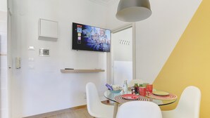 A modern dining area with a glass table, white chairs, and a mounted TV displaying a show. - Furio Camillo Studio - Metro A - Netflix (Rome)
