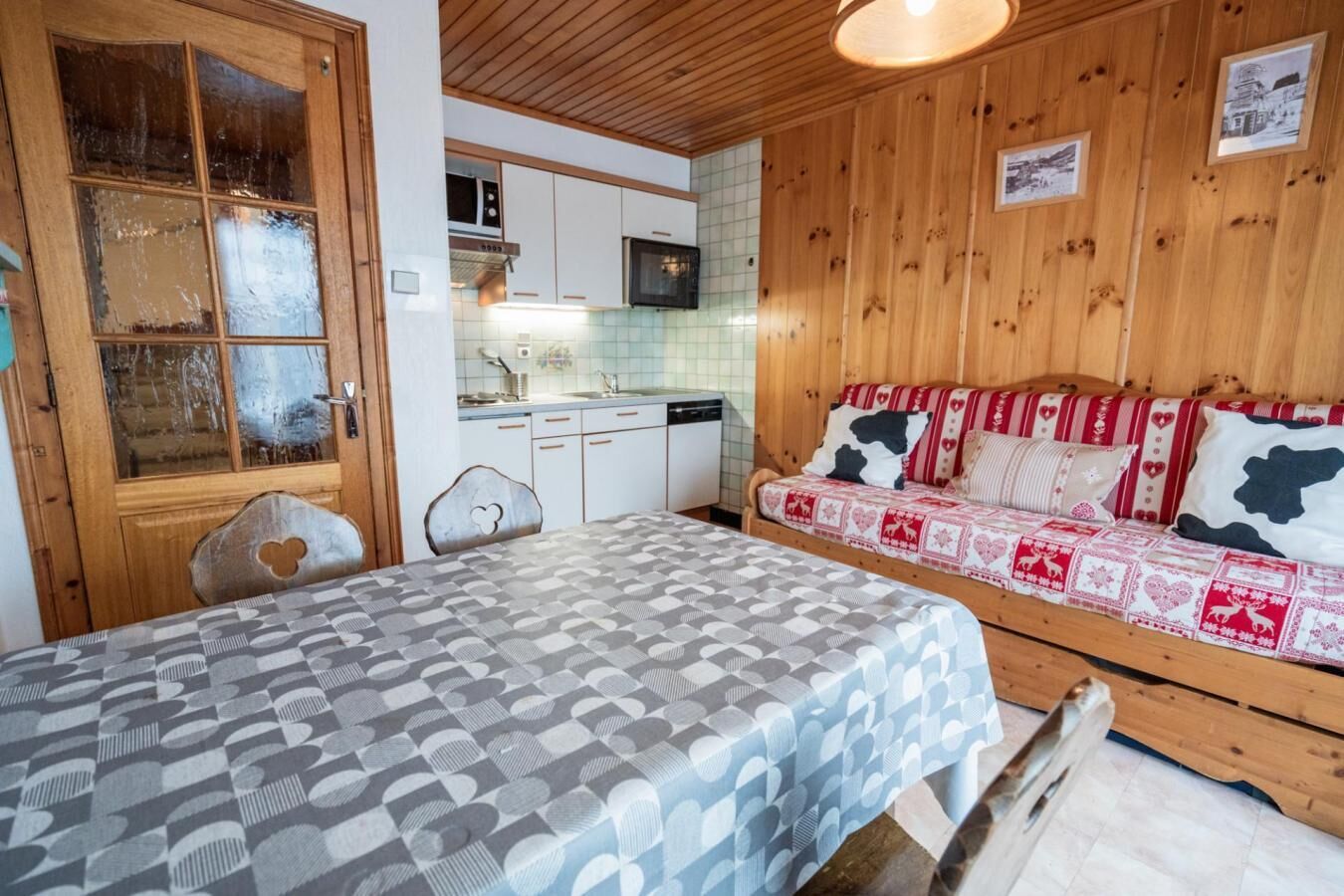 Una habitación acogedora con cama, cabecero de madera, una pequeña kitchenette y una puerta de madera con panel de vidrio.