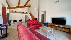 Un ampio soggiorno con un divano in pelle rossa, un tavolino in legno e una TV a schermo piatto su un supporto in legno. Una scala conduce al piano superiore, e ci sono due poltrone nella stanza.