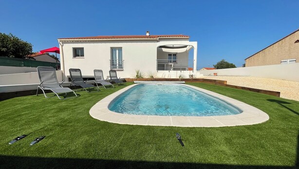 Una piscina rettangolare con bordo bianco, circondata da erba sintetica.
