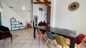 Zona pranzo con un tavolo lungo e sedie colorate, una scala e una sveglia a parete.