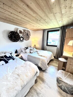Une chambre confortable avec deux lits, un plafond en bois, une grande fenêtre et une petite table.