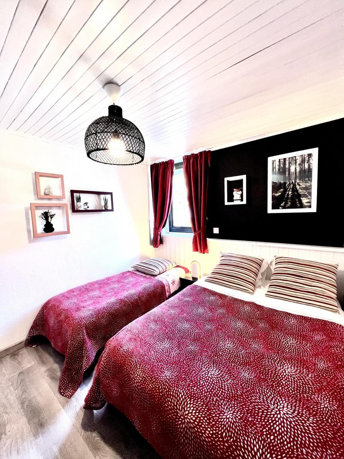 Une chambre avec deux lits, une décoration murale en noir et blanc, un luminaire suspendu et une fenêtre avec des rideaux rouges.