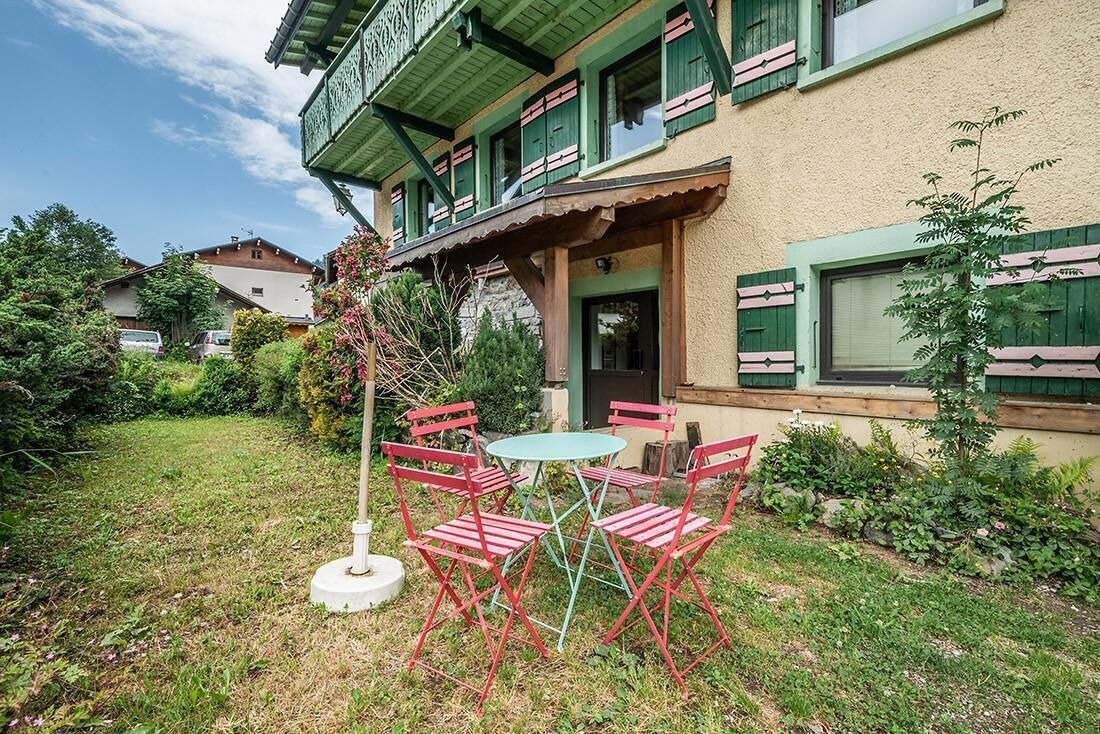 Un immeuble à la façade verdoyante, doté d’un balcon et d’un petit espace jardin avec une table et des chaises.