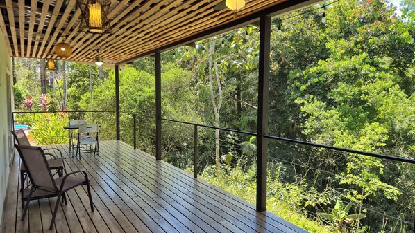 A wooden deck with a table and chairs, overlooking a dense forest.