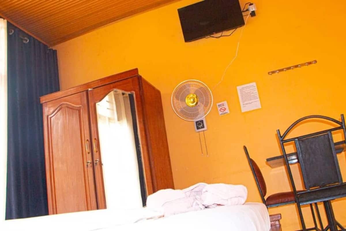 Um quarto com cama, guarda-roupa de madeira, ventoinha e uma cadeira.