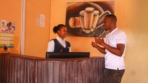 A reception area with a wooden reception desk, a receptionist, and a guest. - Hirwa Avenir (Kigali)