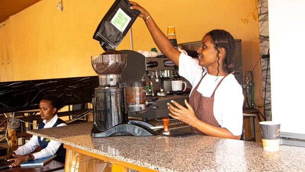 A coffee shop with a barista preparing a drink, a coffee machine, and a counter. - Hirwa Avenir (Kigali)