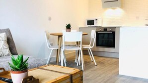 A modern living space with a sofa, a dining table with chairs, a kitchen area with a microwave and oven, and a potted plant. - Beautiful One Bedroom Apartment with additional Sofa Bed, Arbroath centre. (Arbroath)
