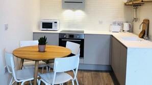 A compact kitchen with a microwave, oven, and sink. There is a small dining table with chairs and a potted plant. - Beautiful One Bedroom Apartment with additional Sofa Bed, Arbroath centre. (Arbroath)