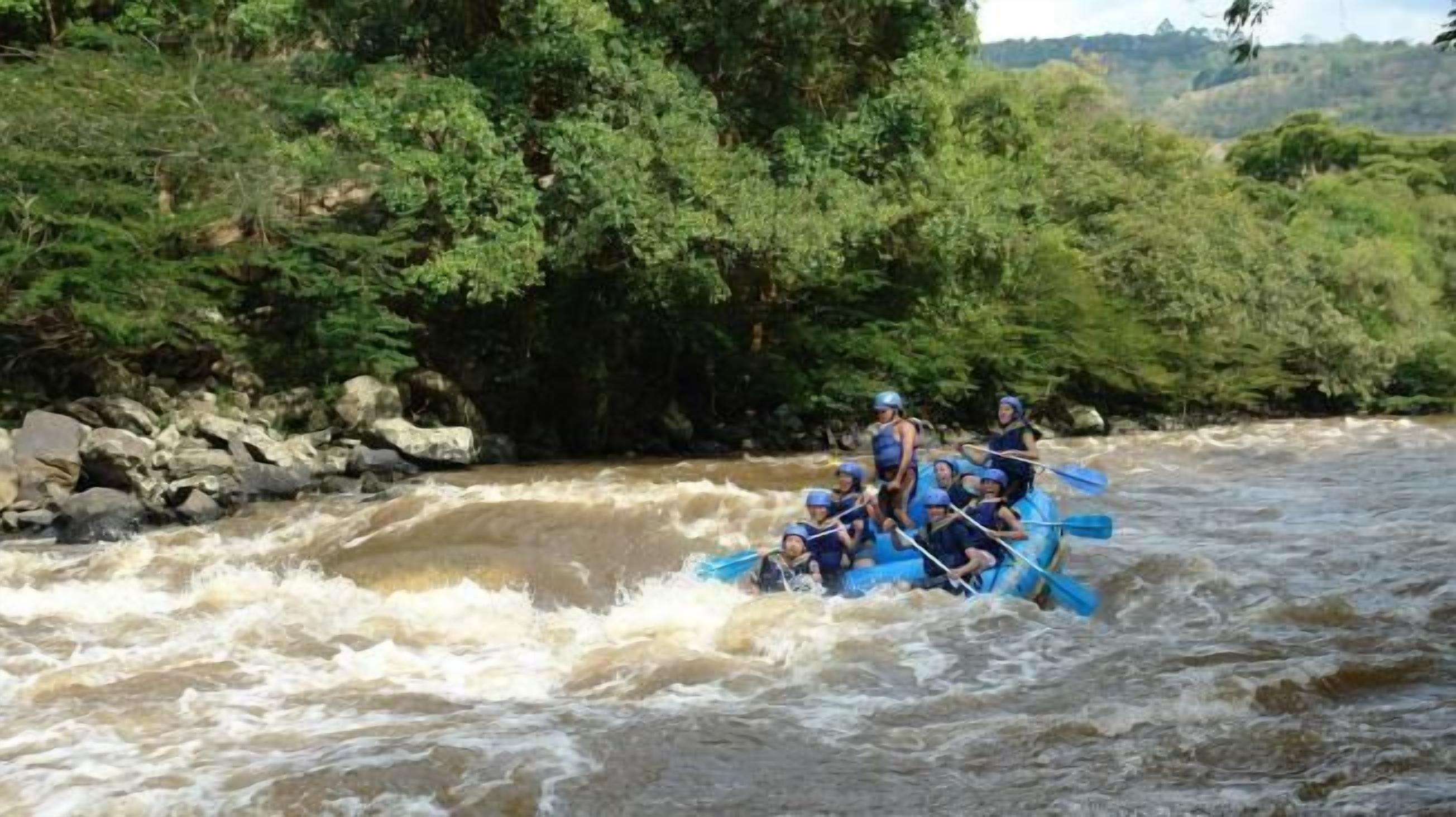 Un groupe de personnes à bord d’un radeau bleu navigue sur une rivière à courant rapide, entourée d’une végétation luxuriante.