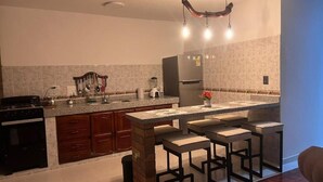 Une cuisine moderne dotée de plans de travail en granit, d’un four encastré, d’un réfrigérateur et d’un coin bar avec des tabourets.