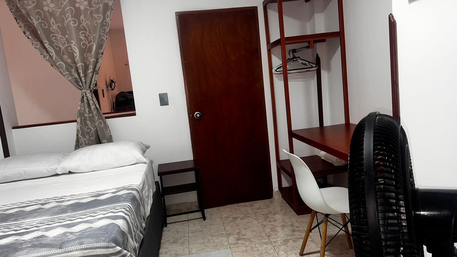 A bedroom with a bed, a desk, a chair, a wardrobe, and a fan.