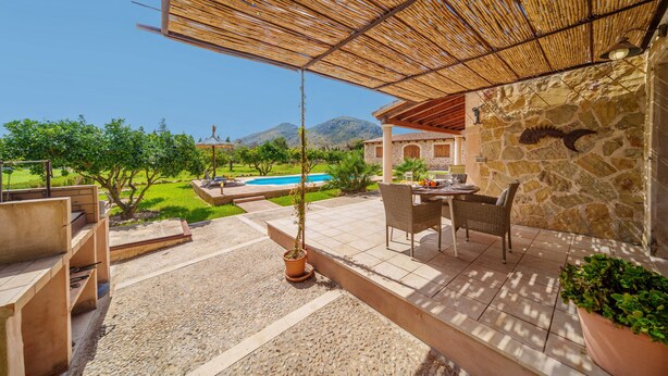 Un'area patio con tavolo e sedie, una piscina sullo sfondo e un paesaggio montuoso.