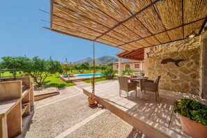 Un espace patio avec une table et des chaises, une piscine en arrière-plan et un paysage montagneux.