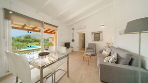 Un soggiorno moderno con un tavolo da pranzo in vetro, un divano grigio e vista su una piscina.