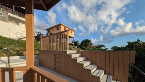 Un escalier en bois menant à un balcon d’où l’on peut admirer un bâtiment et des arbres.