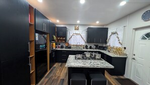 Une cuisine moderne avec des meubles de couleur sombre, un îlot central doté d’un plan de travail en granit et une cuisinière encastrée.
