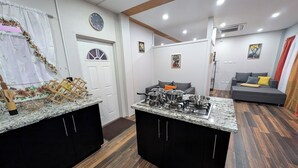 Une cuisine moderne avec des comptoirs en granit, des armoires noires et un îlot central doté d’une cuisinière. On y trouve également un coin repas avec un canapé gris et une petite table.