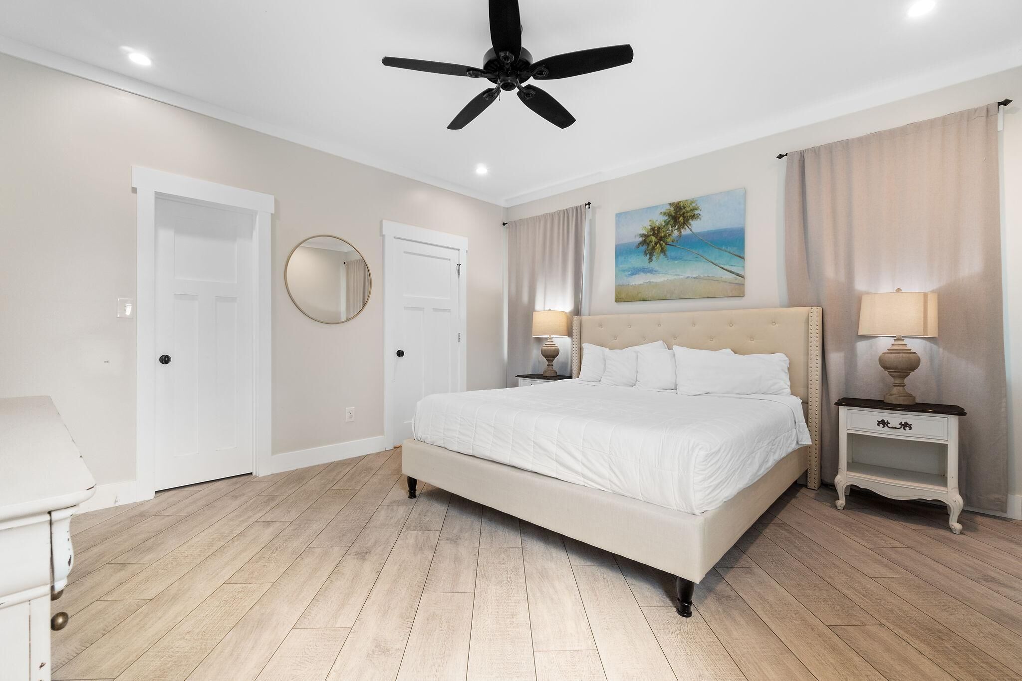 Una camera da letto con un letto, una ventola a soffitto, un quadro raffigurante una spiaggia e due comodini con lampade.