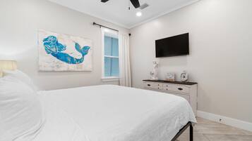 A bedroom with a bed, a ceiling fan, a wall-mounted TV, a window with blinds, and a decorative piece on the dresser.