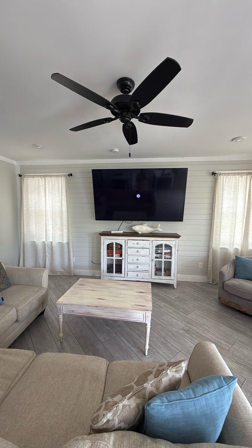 A living room with a ceiling fan, a flat-screen TV, a white cabinet, and two sofas.