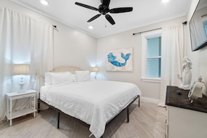 A bedroom with a bed, nightstands, a ceiling fan, a window with blinds, and a wall-mounted TV. - Beach Please (Gulf Shores)