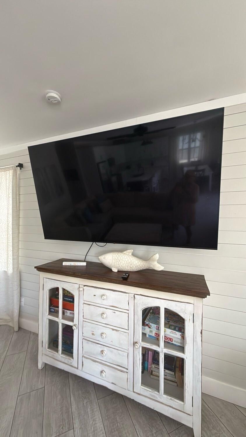 A flat-screen TV mounted on a white wall above a wooden cabinet with drawers and glass doors.