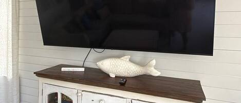Seinälle asennettu litteä näyttö, joka on kiinnitetty valkoiseen seinään. Sen alla on puinen kaappi, jossa on laatikoita ja lasiovet.
