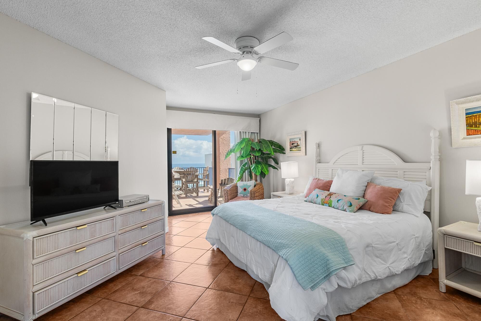 Une chambre à coucher avec un lit, un téléviseur, un ventilateur de plafond et une vue sur l’extérieur.