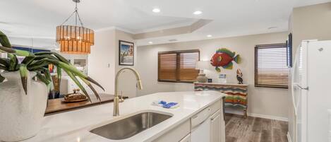 A modern kitchen with a white countertop, stainless steel sink, and a hanging pendant light.