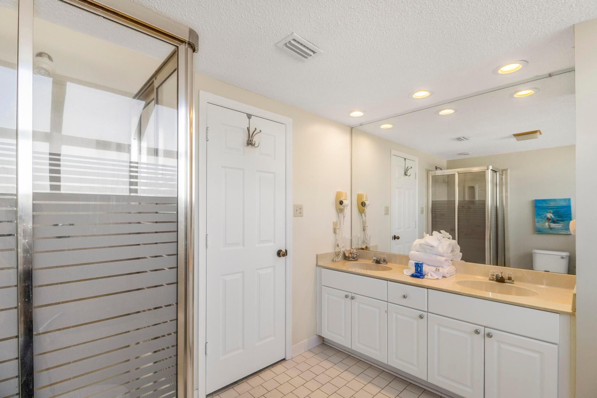 A modern bathroom with a glass shower enclosure, white cabinetry, a large mirror, and a tiled floor.