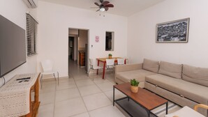 Een woonkamer met een bank, een salontafel, een televisie, een plafondventilator, een eethoek met stoelen en een tafel, en een lijst met een afbeelding aan de muur.