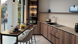 A modern kitchen with a built-in oven, a sink, and a countertop. There is a dining area with a table and chairs. - Villa Ada: Elegant Villa with Private Pool & Mount Etna Views (Taormina)