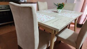 A dining table with floral placemats, beige upholstered chairs, and a potted plant.