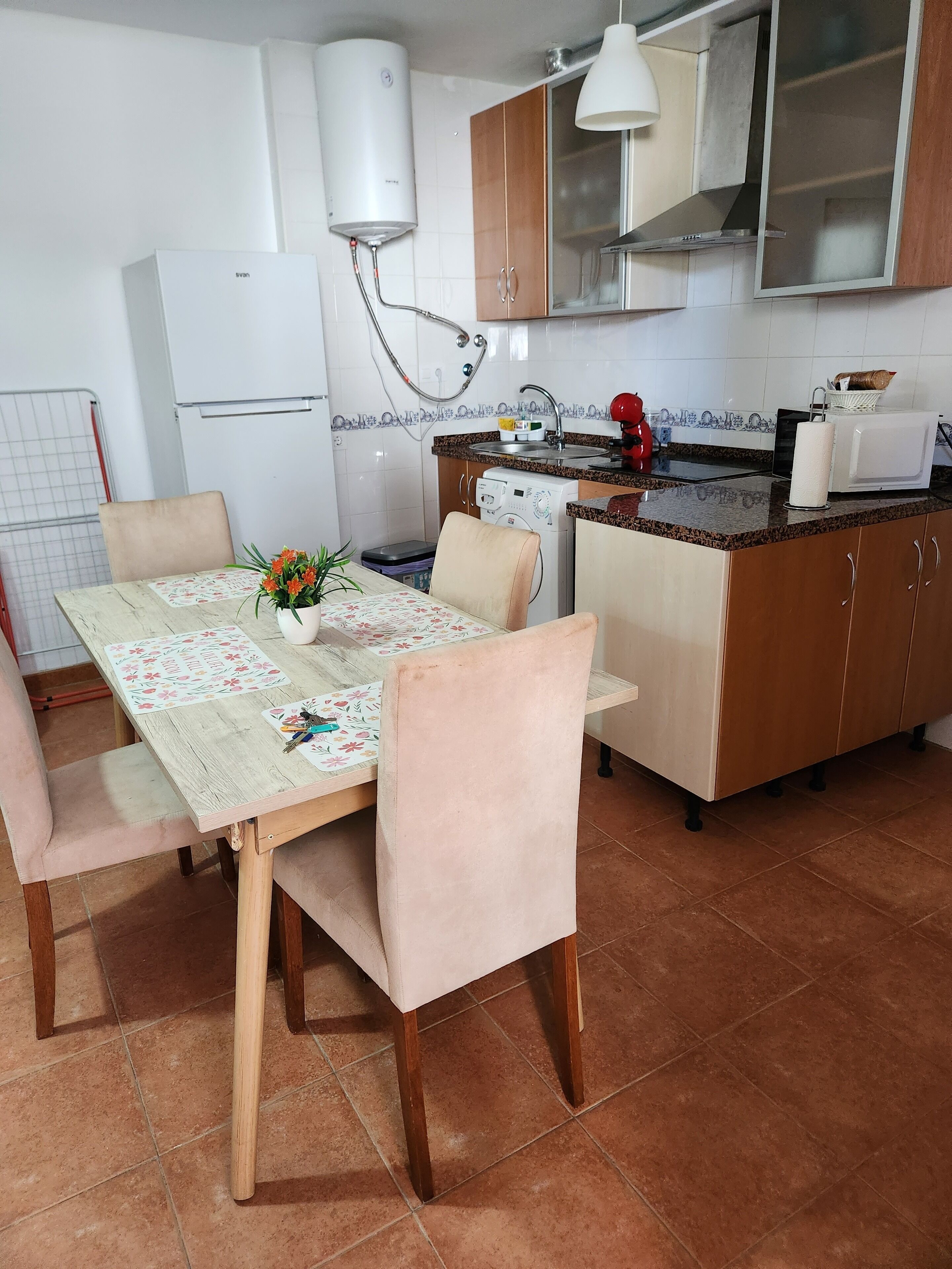 A compact kitchen with a dining table, chairs, a washing machine, a microwave, and a water heater.