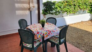 A patio with a table and chairs, a potted plant, and a white wall with a window.