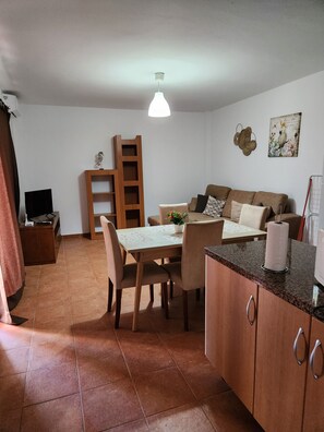 Un espacio habitable compacto con comedor, sofá, televisor y una escalera.