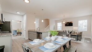 Una cocina moderna con comedor listo para una comida, que incluye una mesa de madera, sillas y un amplio ventanal.