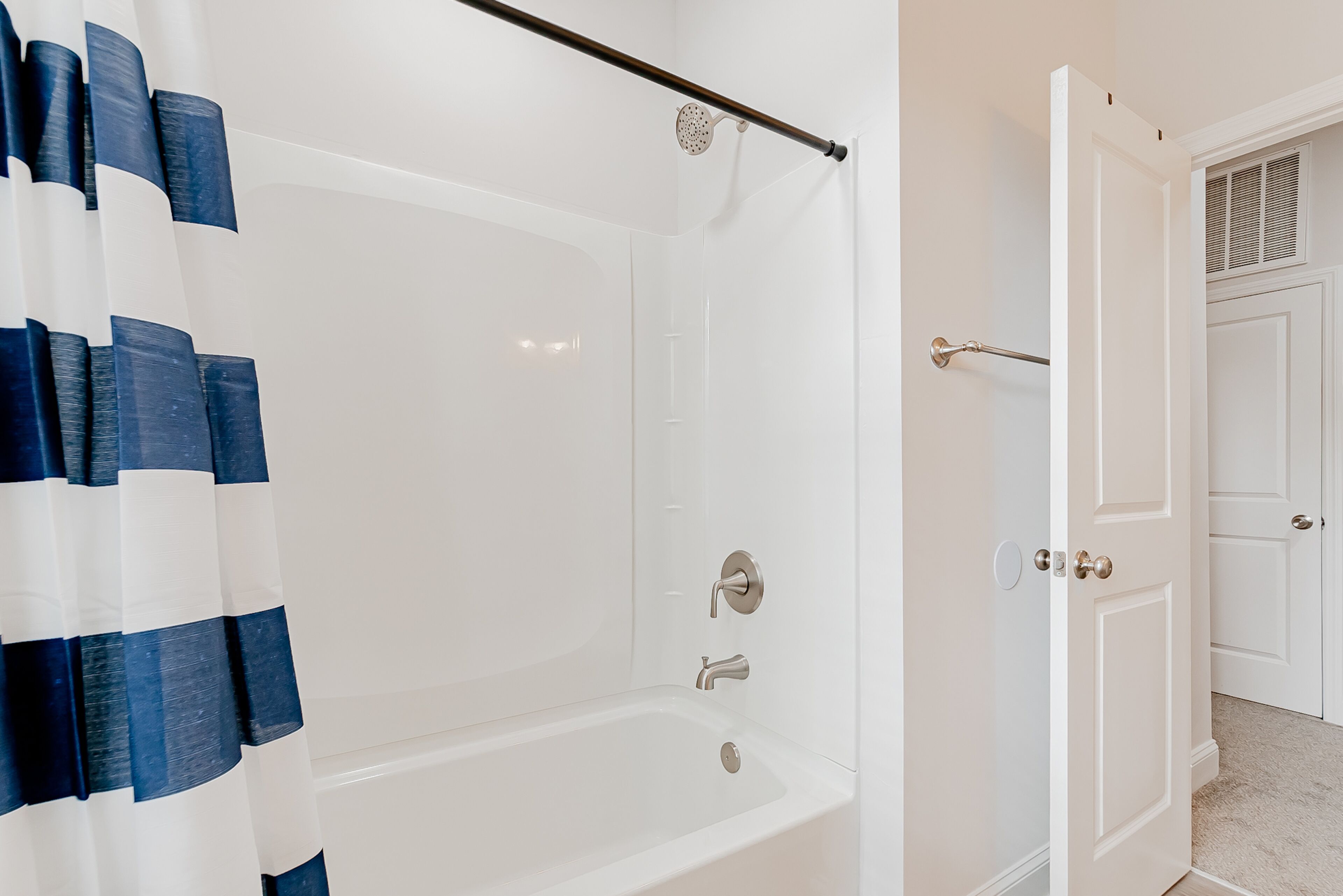 A bathroom with a bathtub, shower curtain, and a door leading to another room.