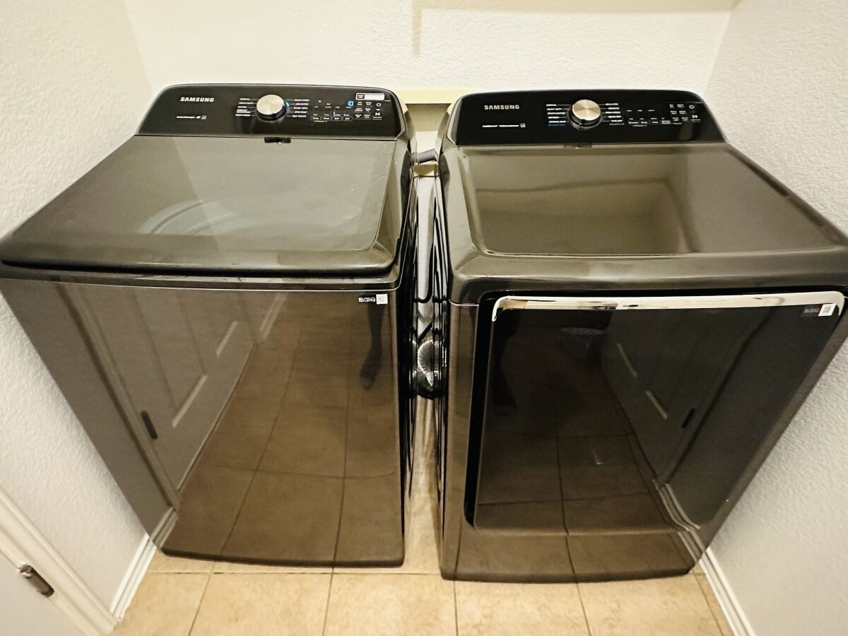 Two front-loading Samsung washing machines in a corner of a room with a tiled floor.