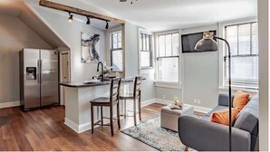 A modern kitchen with a built-in island, a dining area with chairs, a ceiling fan, and a large window with blinds. - Dauphin Darling 4 Units  (Mobile)