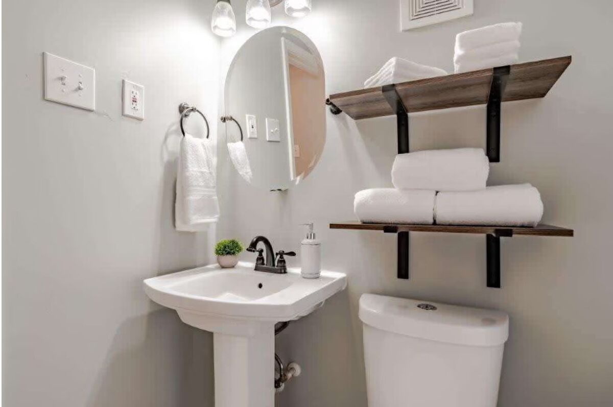 A bathroom with a white sink, a mirror, a toilet, and a towel rack with towels.